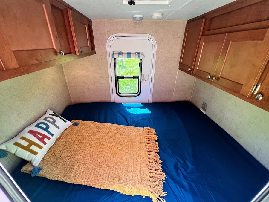 door open to blue interior.|Cozy RV rental interior: bed with 'HAPPY' pillow