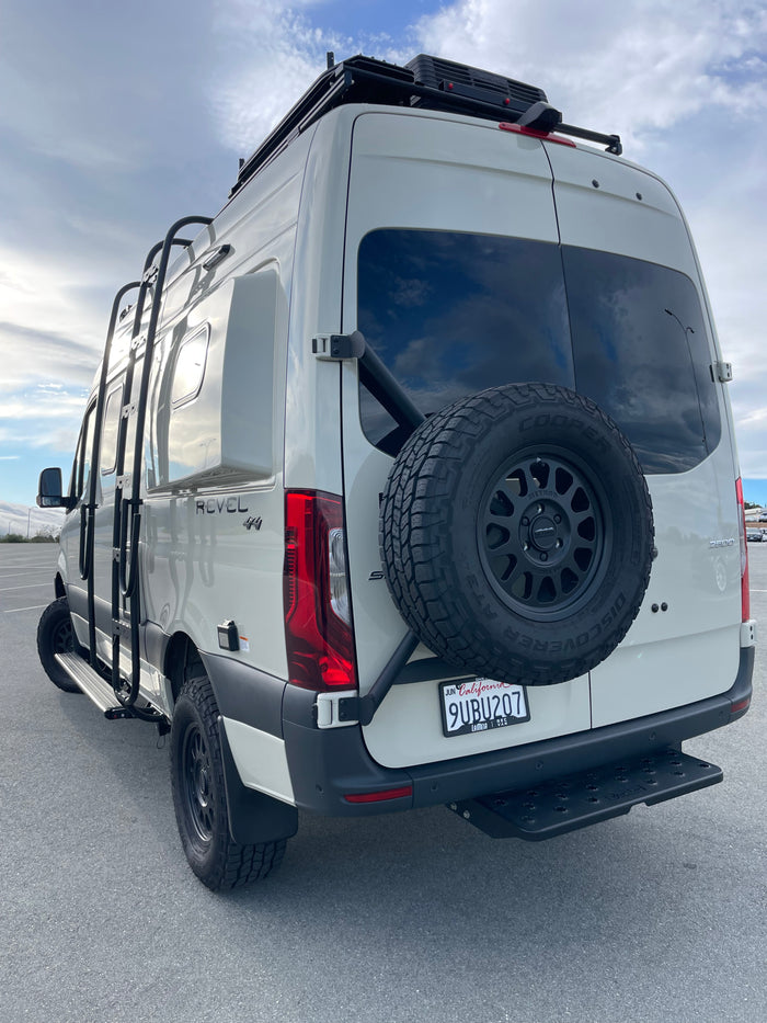 This white Winnebago Revel camper van, a great RV rental option, features a roof rack, ladder, and rear spare tire.