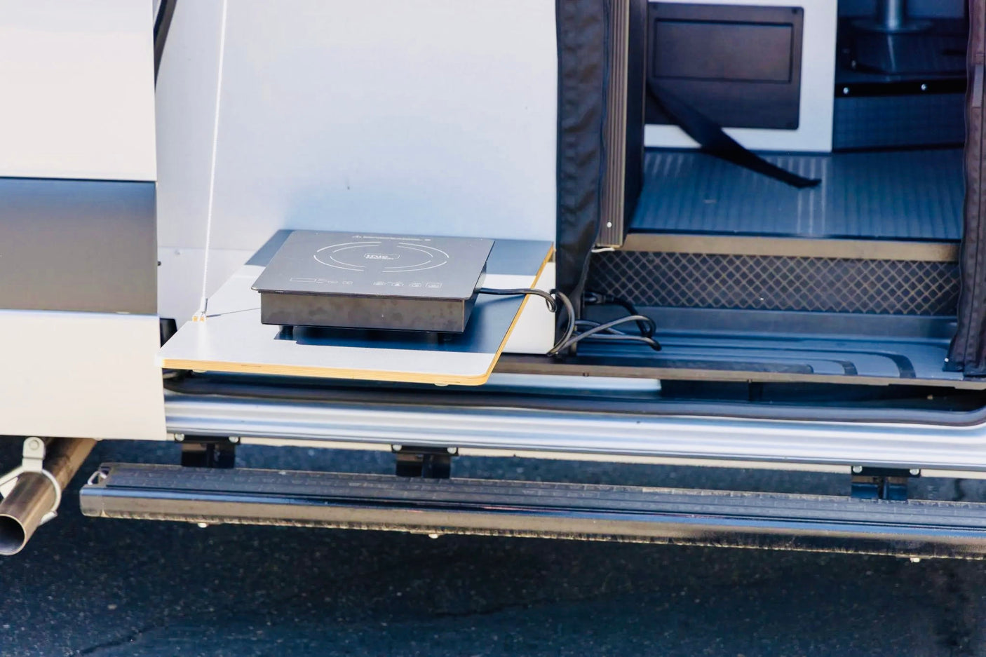 RV rental: An outdoor kitchen with a black induction cooktop on a pull-out shelf, perfect for campervan cooking.