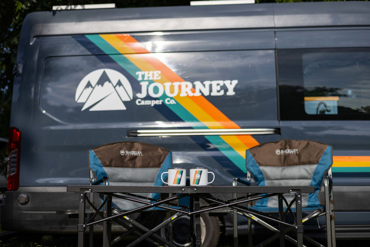 ready for your adventure.|A dark blue "The Journey Camper Co." RV rental van with colorful stripes is parked in a sunny