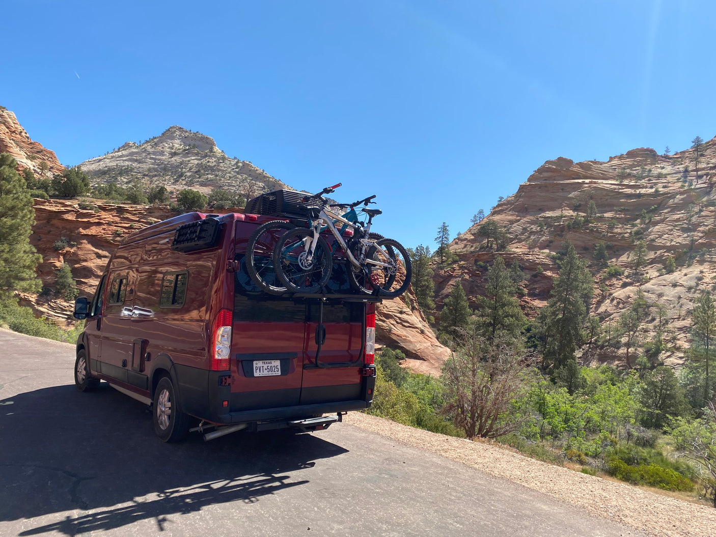 Adventure-ready RV rental with bikes. A red camper van is parked on a scenic road, surrounded by majestic layered mountains.