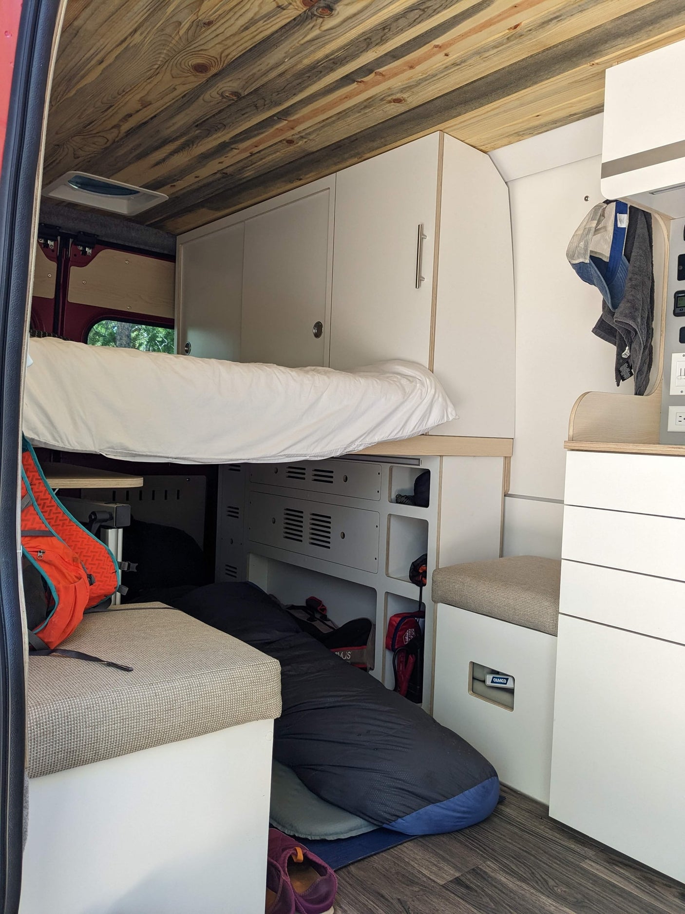 ready for trails.|Red RV rental van on a dirt road amidst majestic red rock formations under a clear blue sky.|RV rental interior featuring a neatly made bed with white bedding