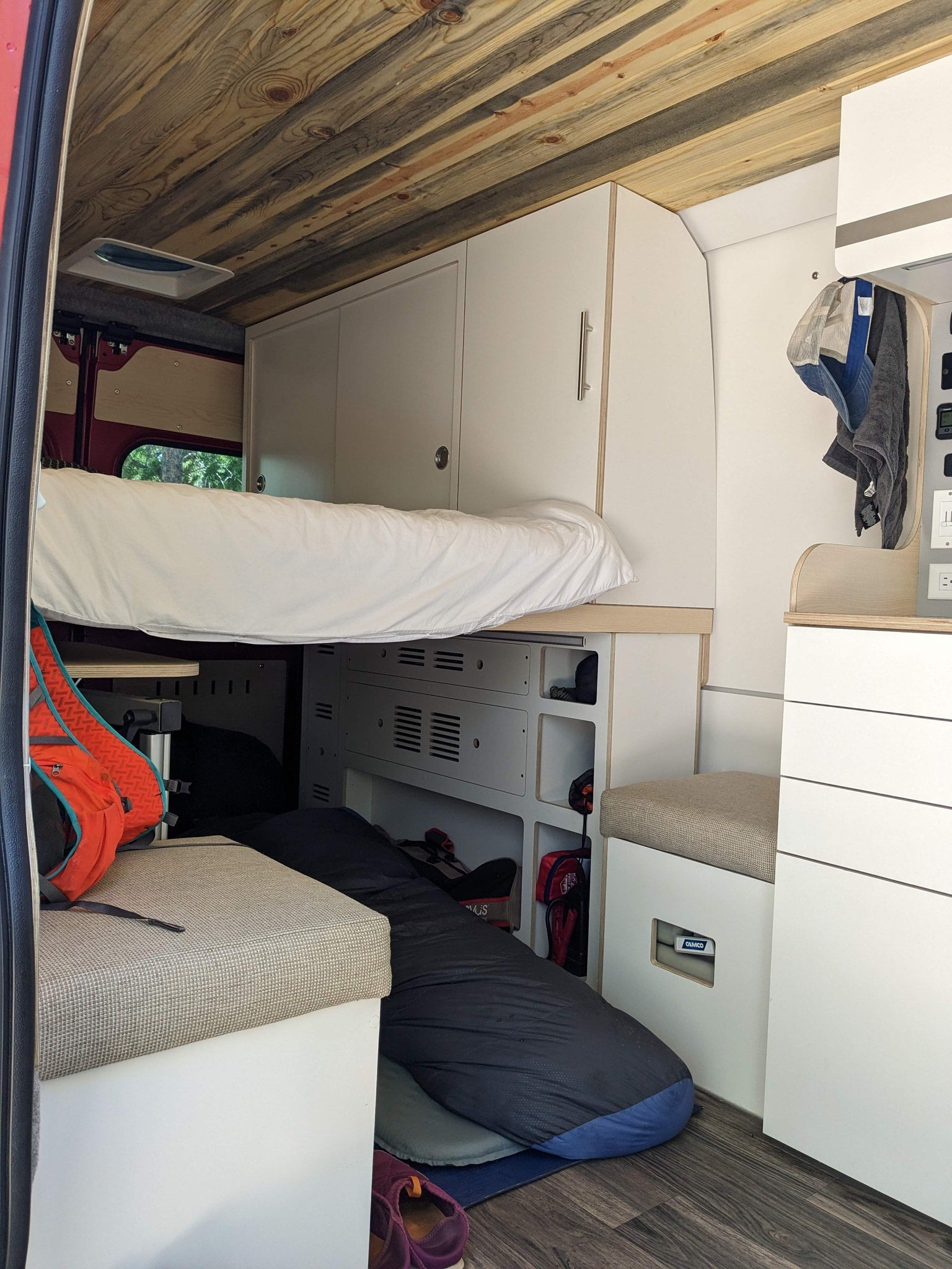 ready for trails.|Red RV rental van on a dirt road amidst majestic red rock formations under a clear blue sky.|RV rental interior featuring a neatly made bed with white bedding