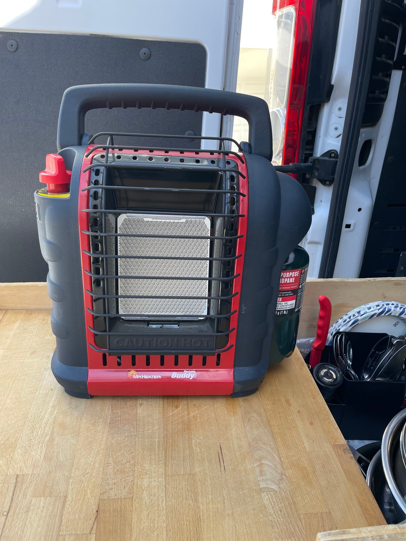 Portable Mr. Heater Buddy propane heater in an RV rental van, on a wooden counter with kitchen items, ready for warmth.