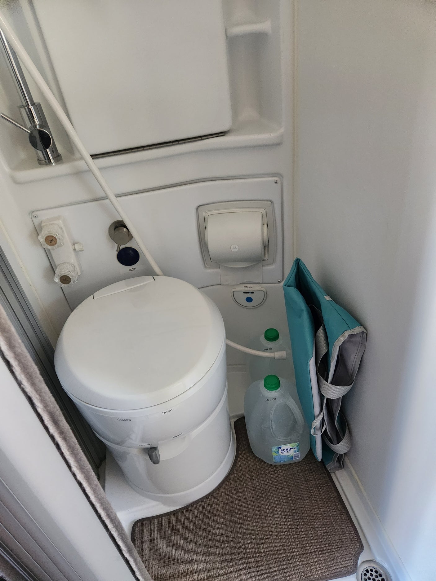 RV rental compact bathroom. Features a white portable toilet, shower controls, and water storage in a functional interior.