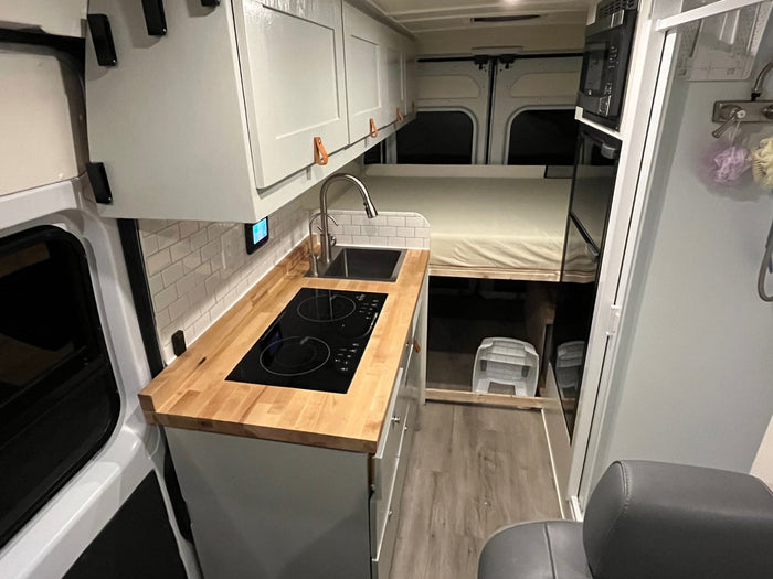 This RV rental's modern interior features a sleek kitchen with cooktop and sink, a raised bed, and smart storage.