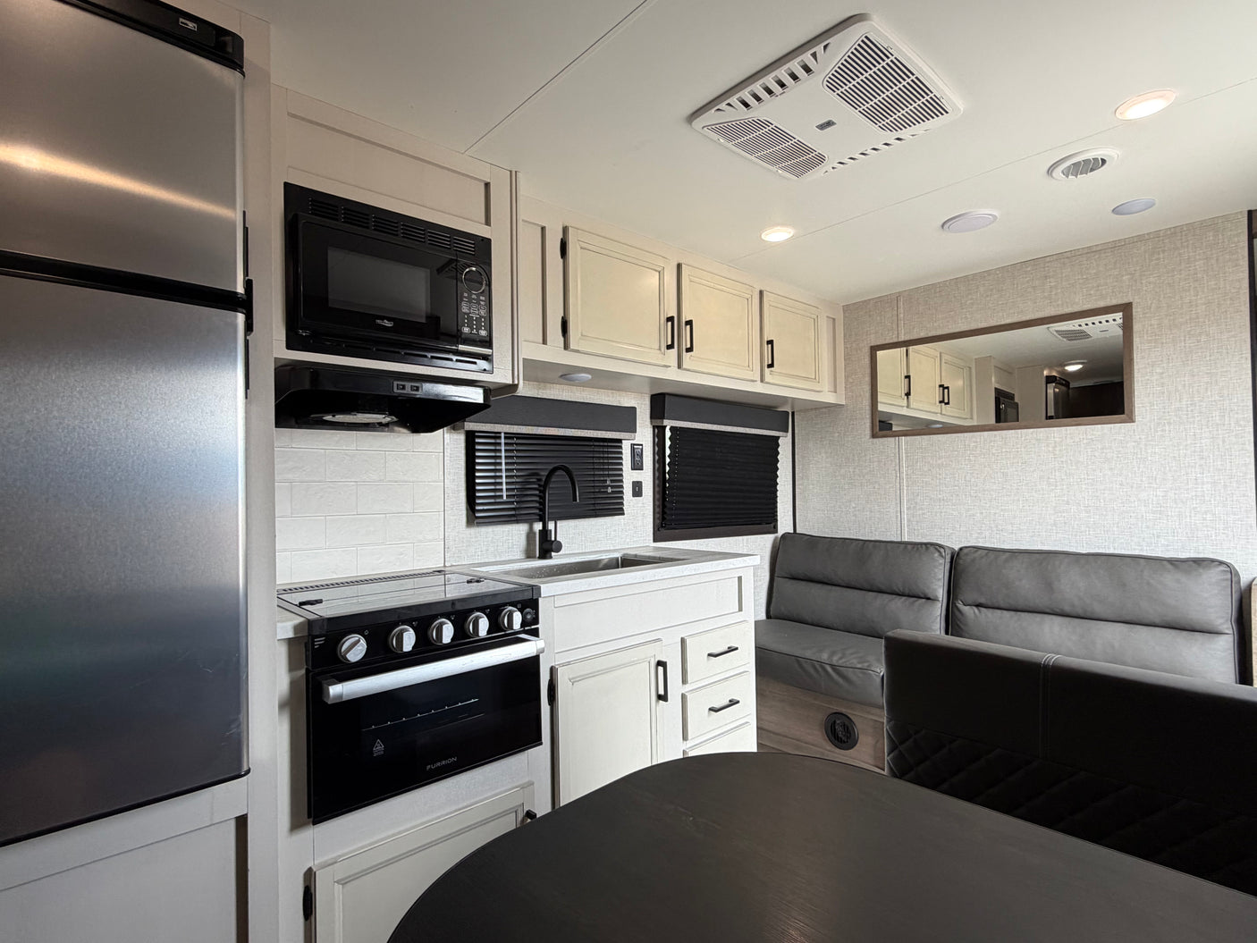 Modern RV rental interior: kitchen with stainless fridge, microwave, stove, sink, and dining area with booth seating.