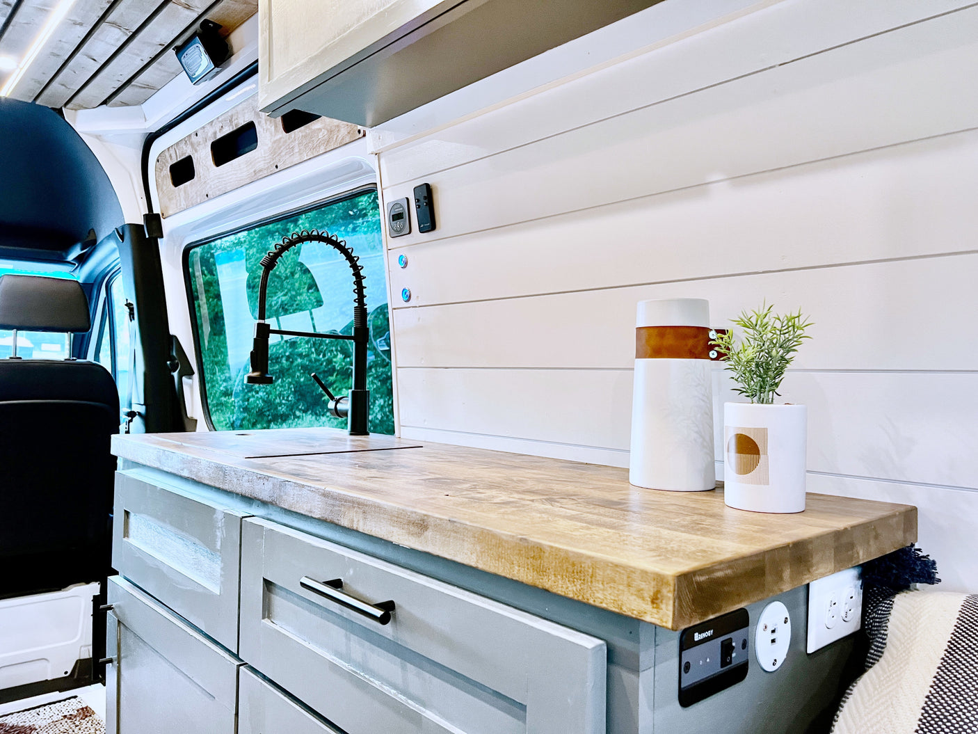 Modern RV rental kitchen in a van conversion, featuring a wooden counter, sink, and integrated controls for comfortable travel.