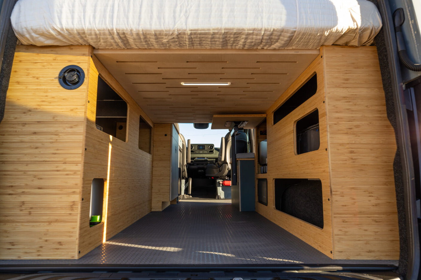 Inside a custom bamboo camper van conversion with rear bed & ample storage, ideal for an rv rental.