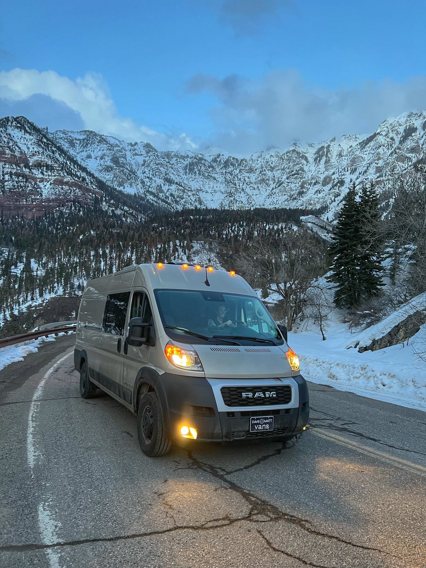 RV rental camper van drives on a curved road through scenic snowy mountains. Ideal for winter travel.