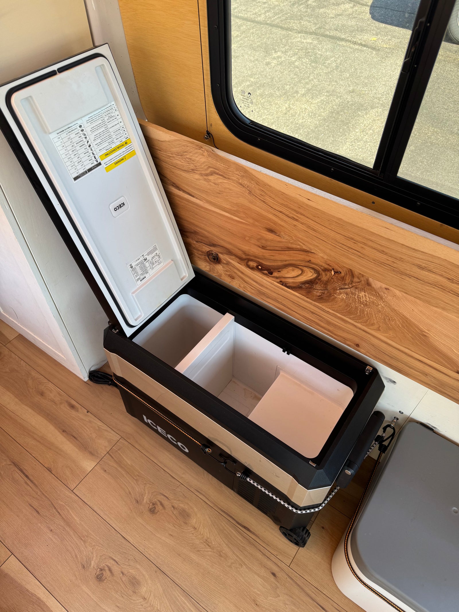 An open ICECO portable fridge/freezer inside an RV rental, showcasing its interior compartments and the vehicle's wood decor.