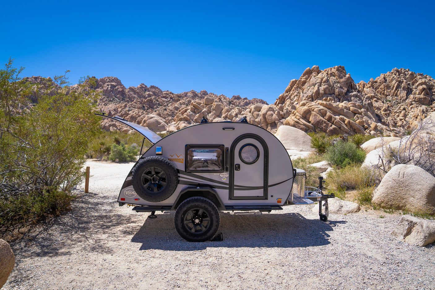 Teardrop camper RV rental parked in a rugged desert landscape with large rock formations and blue sky, ready for adventure.