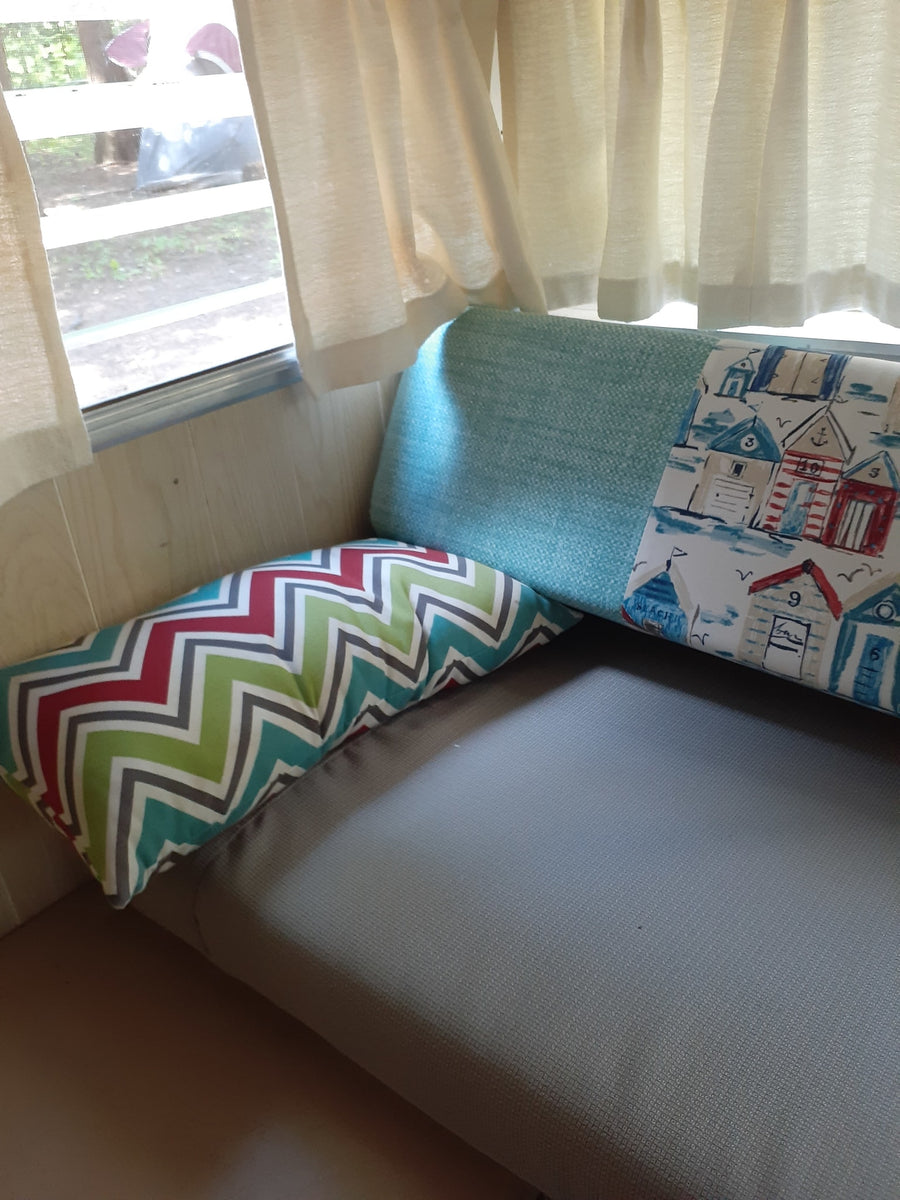 Cozy RV rental interior with patterned pillows on a grey sofa by a window with curtains.