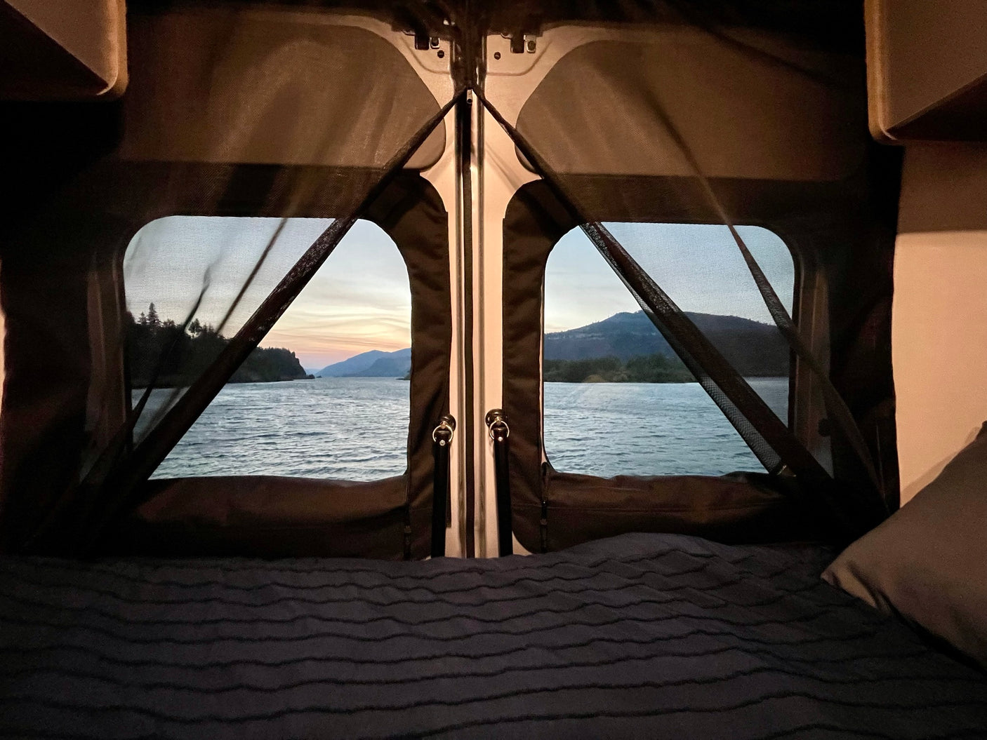 Peaceful rv rental view from bed: tranquil water, mountains, and twilight sky through screened back doors.