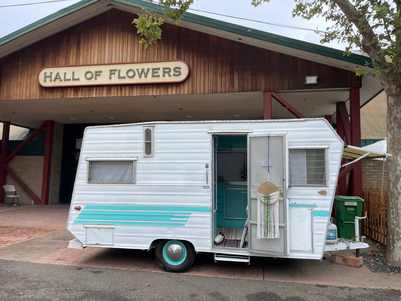 Vintage white & teal RV rental outside "Hall of Flowers". Open door reveals retro interior design.