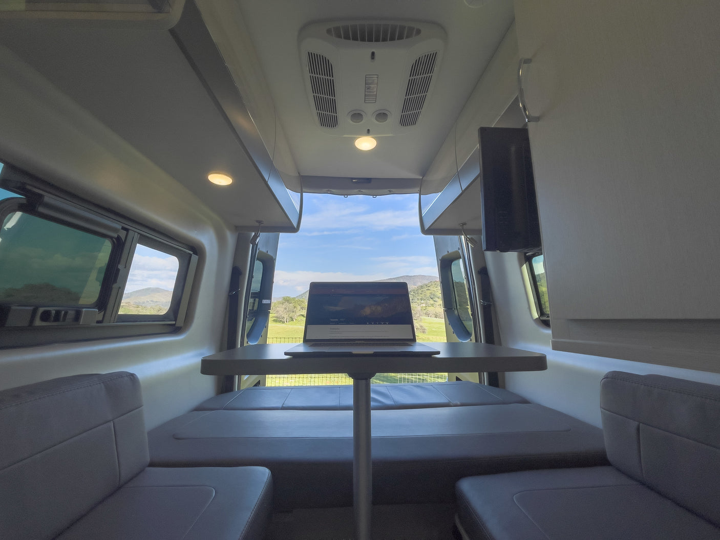 Modern RV rental interior: laptop on dinette table, perfect for remote work with scenic views of nature.