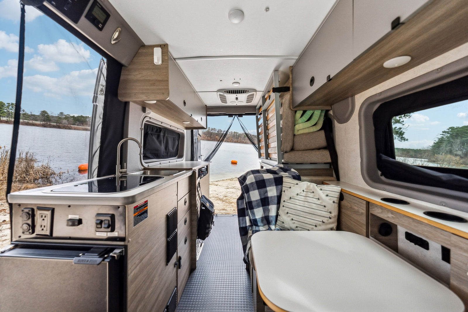 parked lakeside for a scenic getaway.|White Winnebago Solis Pocket camper van for rv rental on gravel