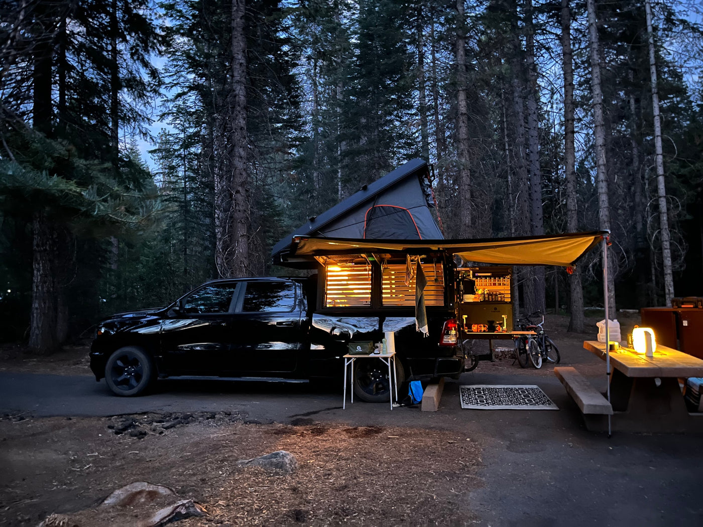 A black truck with an illuminated truck camper and outdoor kitchen at a cozy forest campsite. A unique RV rental alternative. — photo 6
