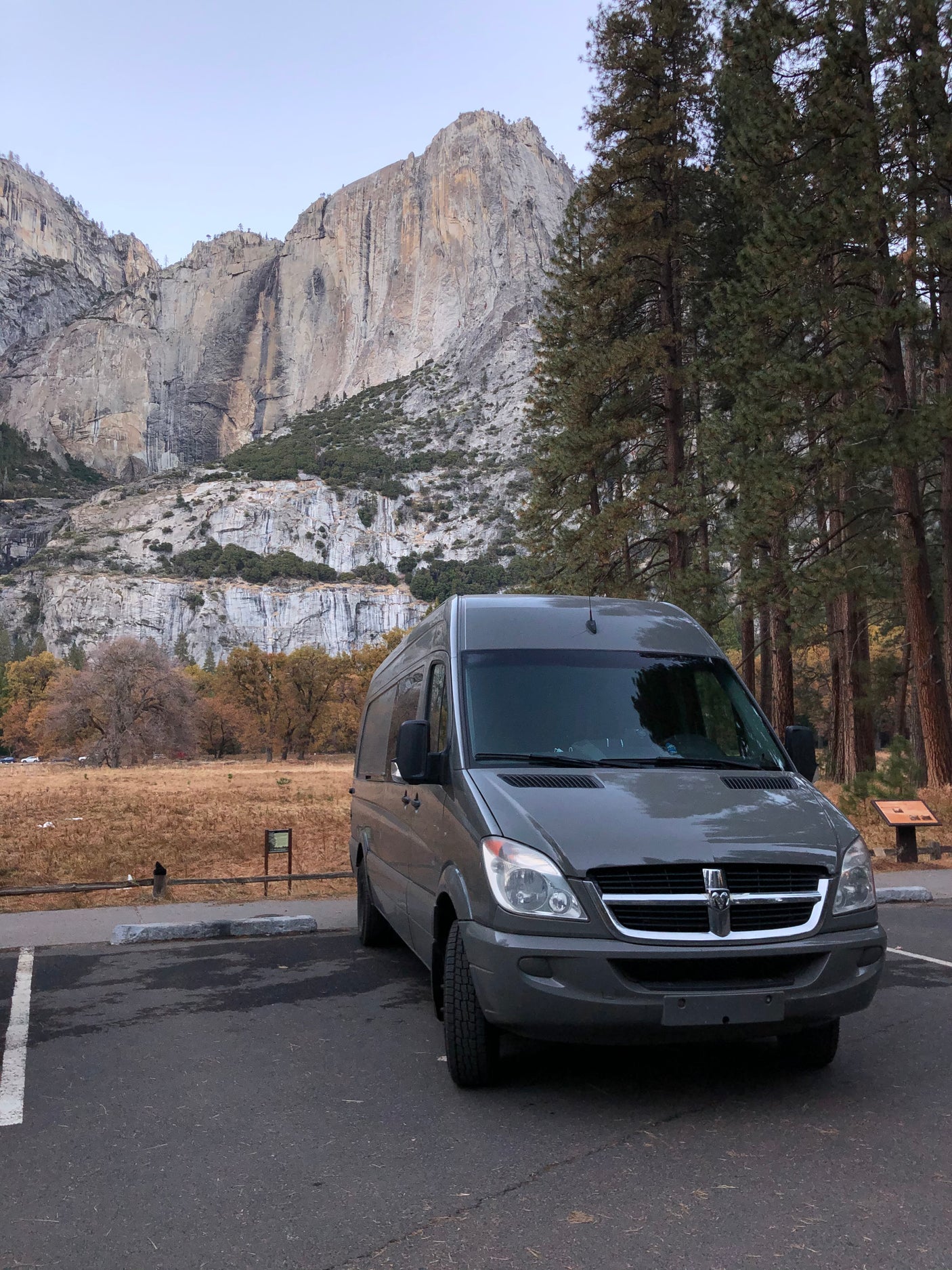 A grey rv rental van is parked in Yosemite National Park, with majestic granite cliffs and autumn-toned meadows.