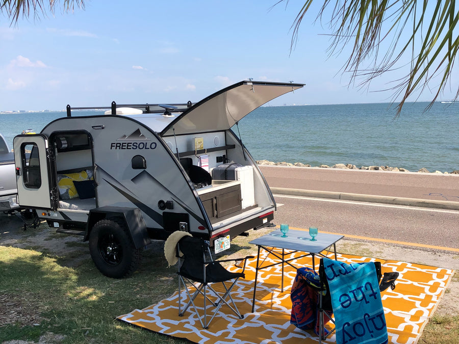 Enjoy beachfront camping with this cozy RV rental. Features an outdoor kitchen and comfy bed, set on a bright mat by the water.
