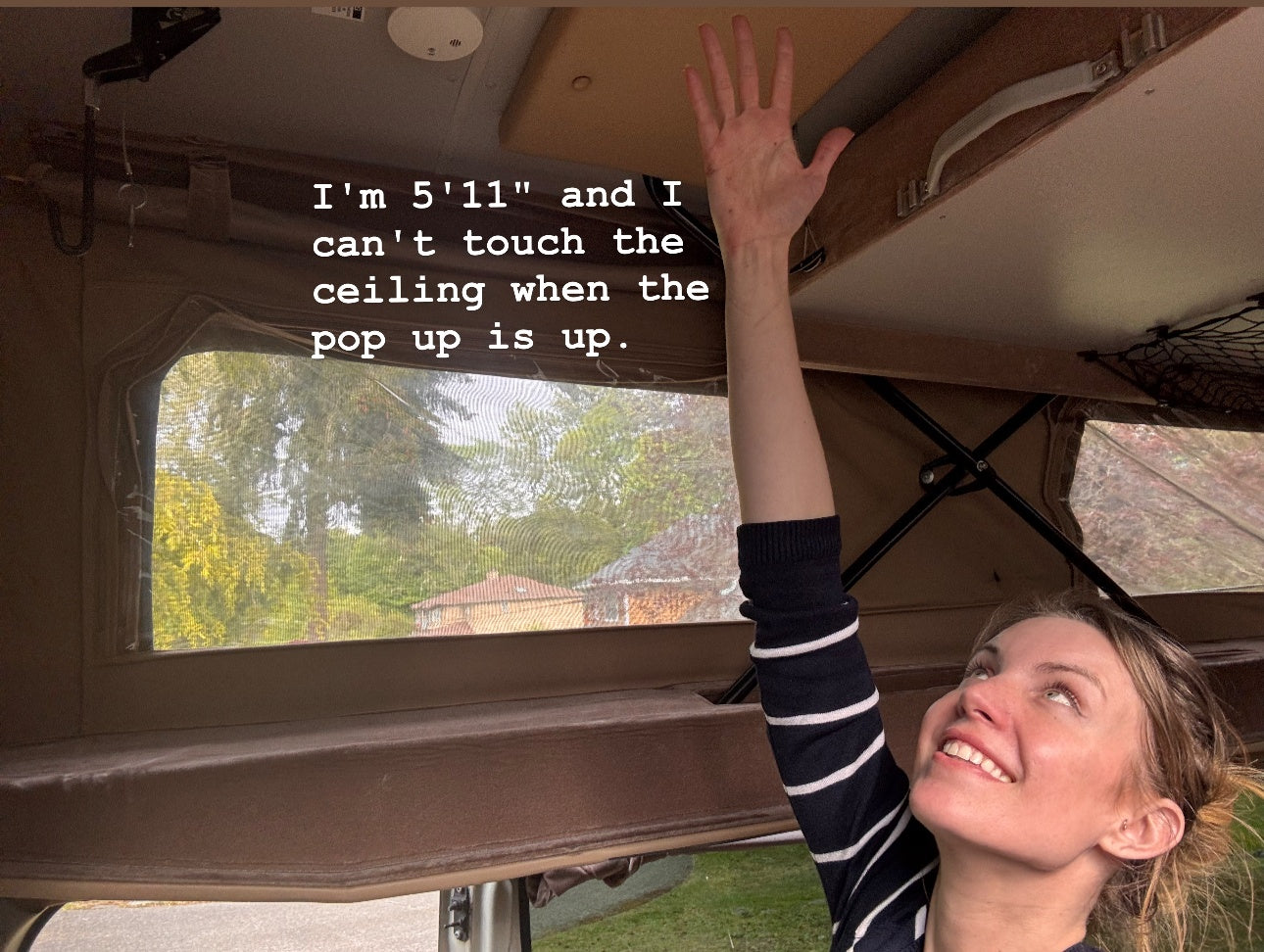 Woman at 5'11" reaches for the high ceiling in a pop-up RV rental, demonstrating ample headroom when extended.