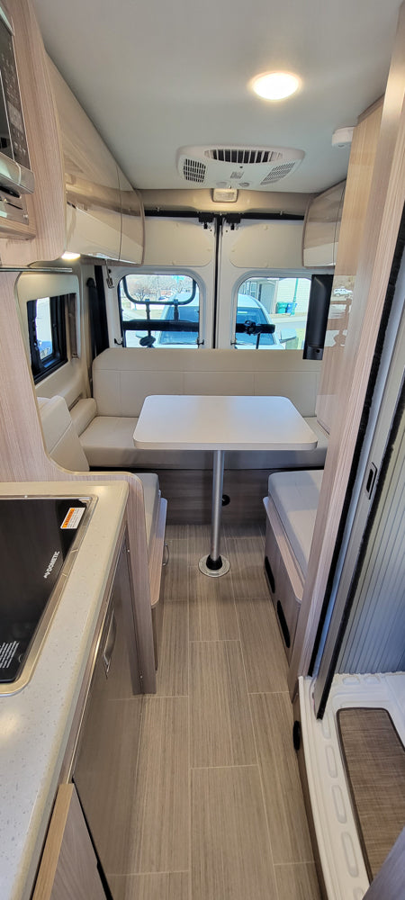 Interior of a modern RV rental, featuring a dinette with bench seating, a compact kitchen, and overhead lighting. Perfect for road trips.