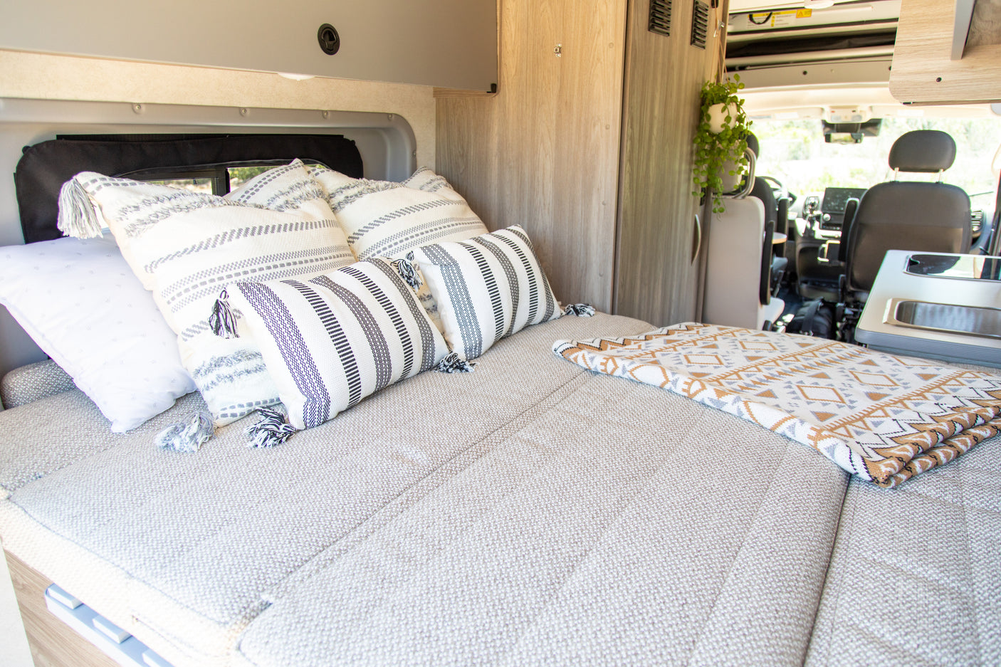 Inviting RV rental interior: a comfy bed with striped and tasseled pillows, and a geometric blanket. Perfect for road trips!