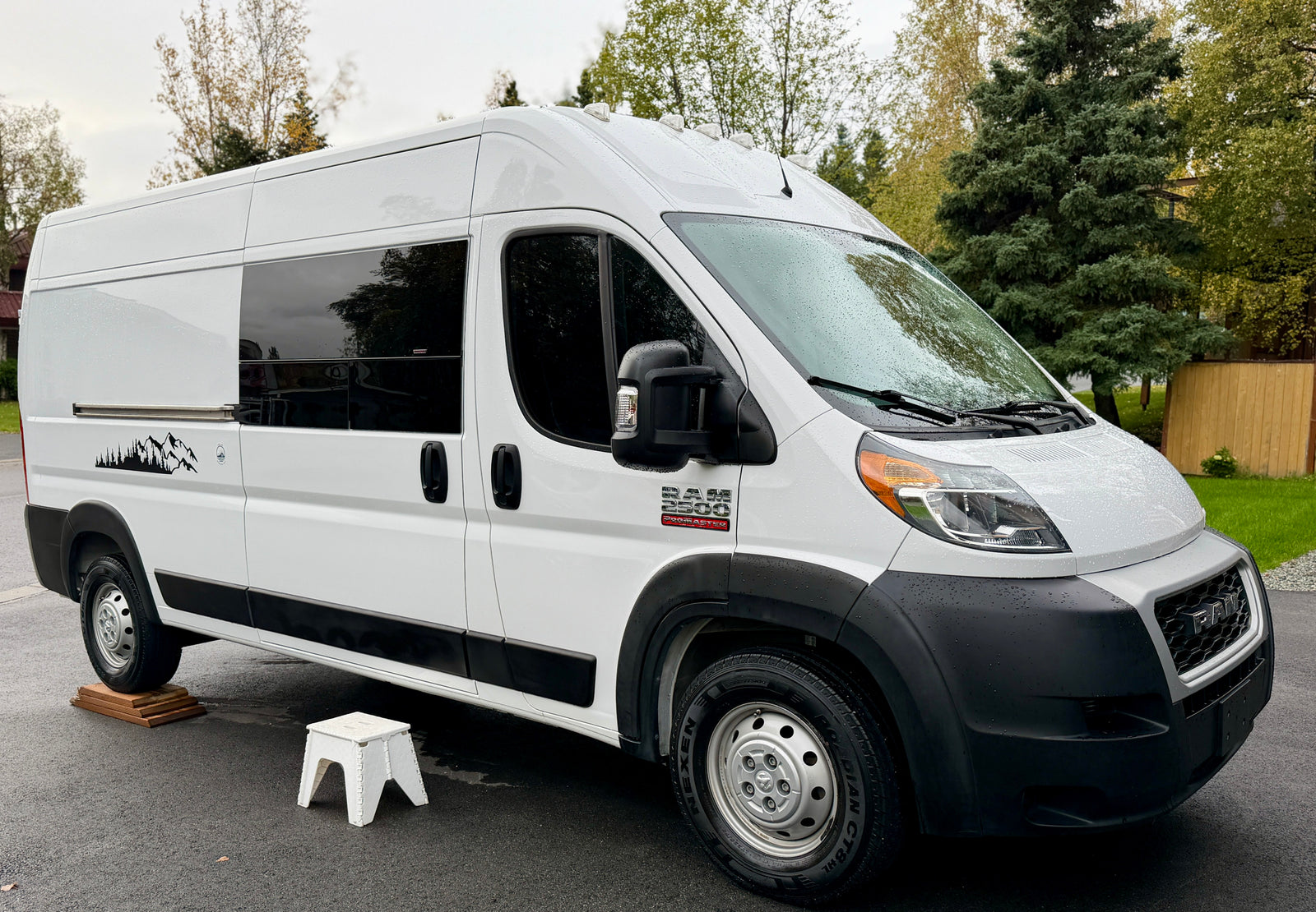 A white Ram Promaster RV rental, equipped as a camper van, parked on leveling blocks outdoors.