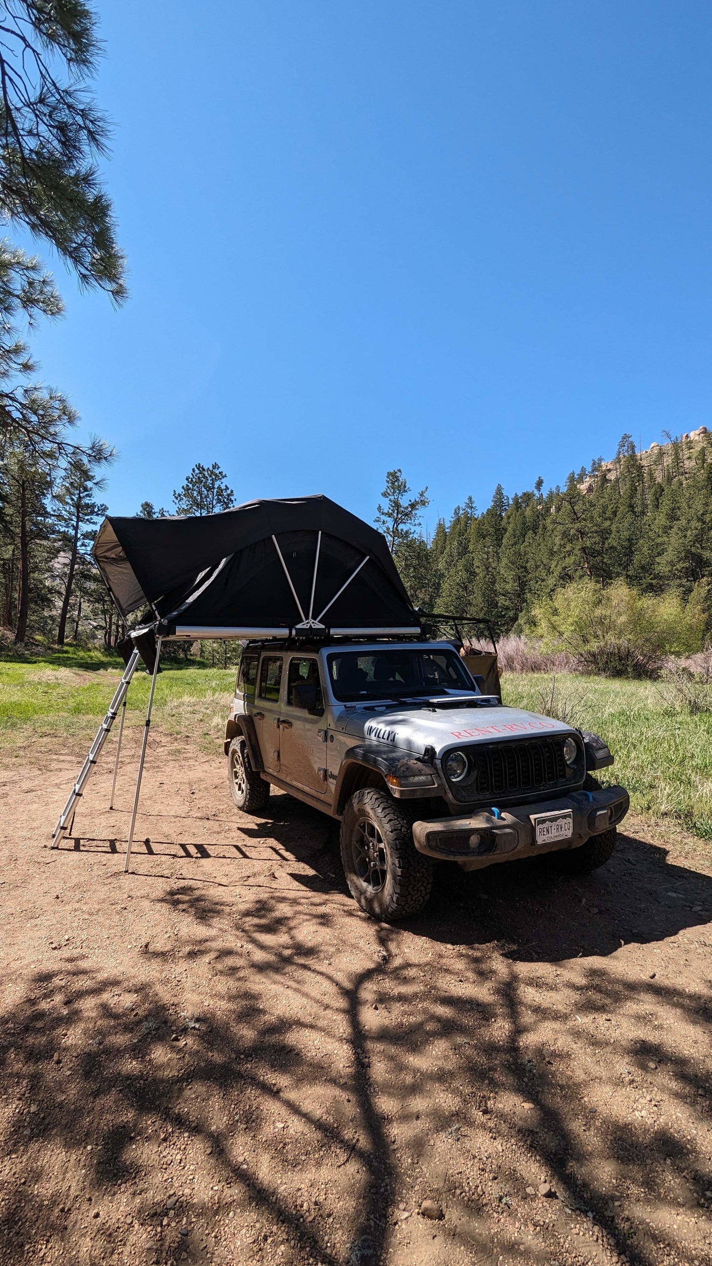 Silver Jeep Wrangler with a rooftop tent deployed, showing its "RENT-RV.CO" branding. An ideal RV rental for outdoor adventures.