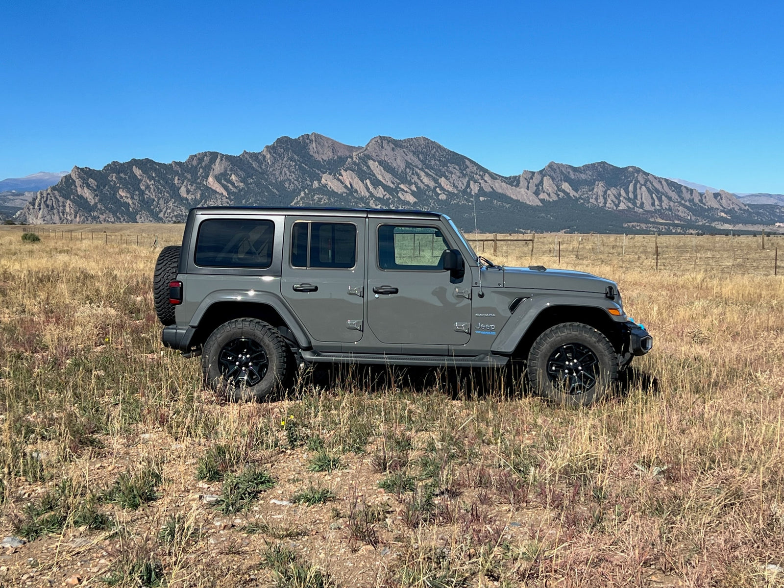 Gray Jeep Wrangler 4xe in a scenic field with mountains (likely Boulder Flatirons).
