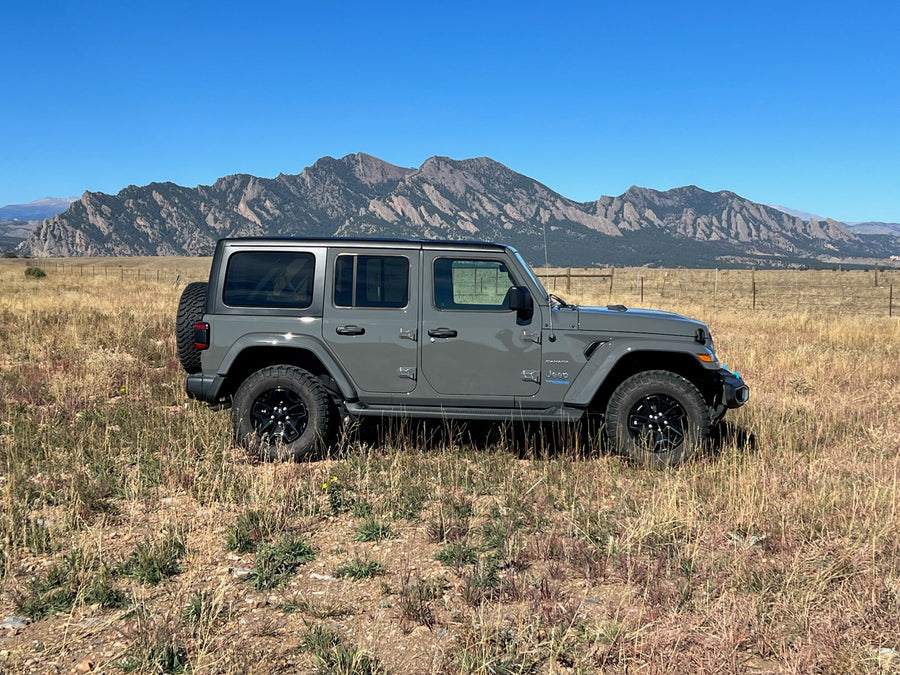 Gray Jeep Wrangler 4xe in a scenic field with mountains (likely Boulder Flatirons).