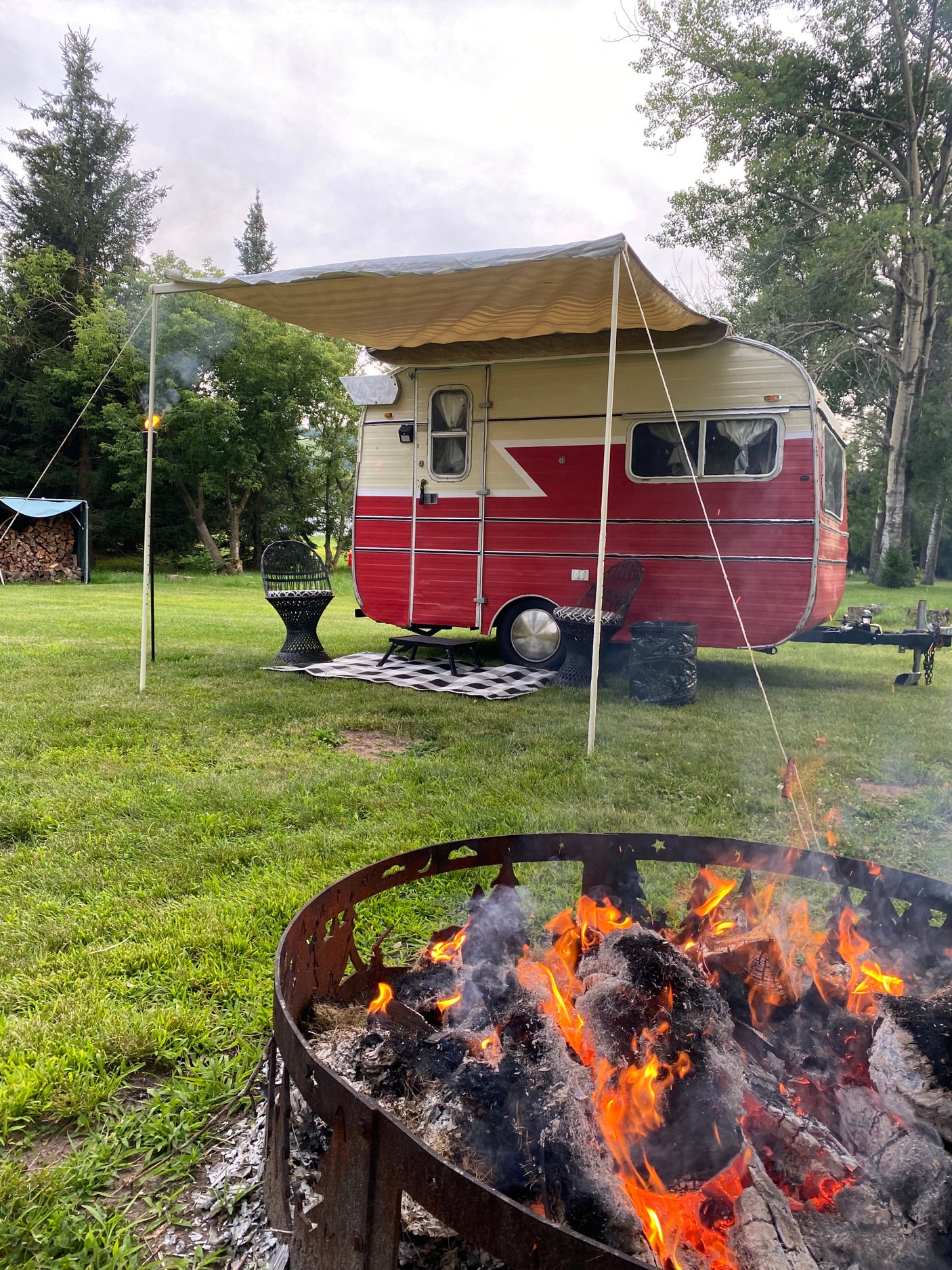 Enjoy a relaxing campout! This RV rental has an awning, comfy chairs, and a warm fire pit in a lush green setting.