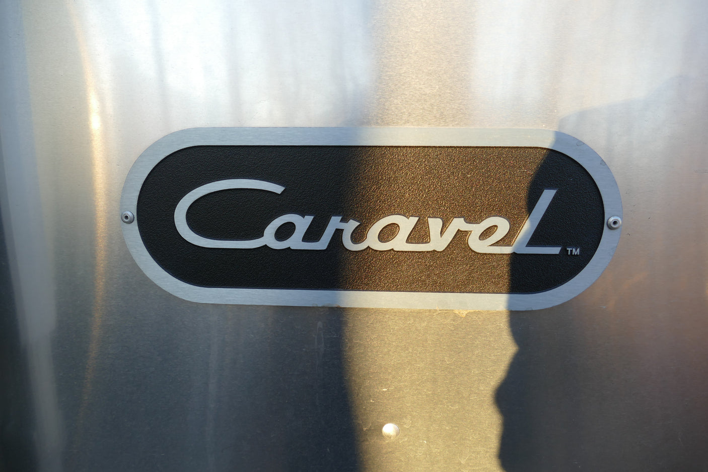 Silver 'Caravel'â„¢ emblem on a black plaque, riveted to a brushed aluminum Airstream travel trailer, ideal for rv rental.