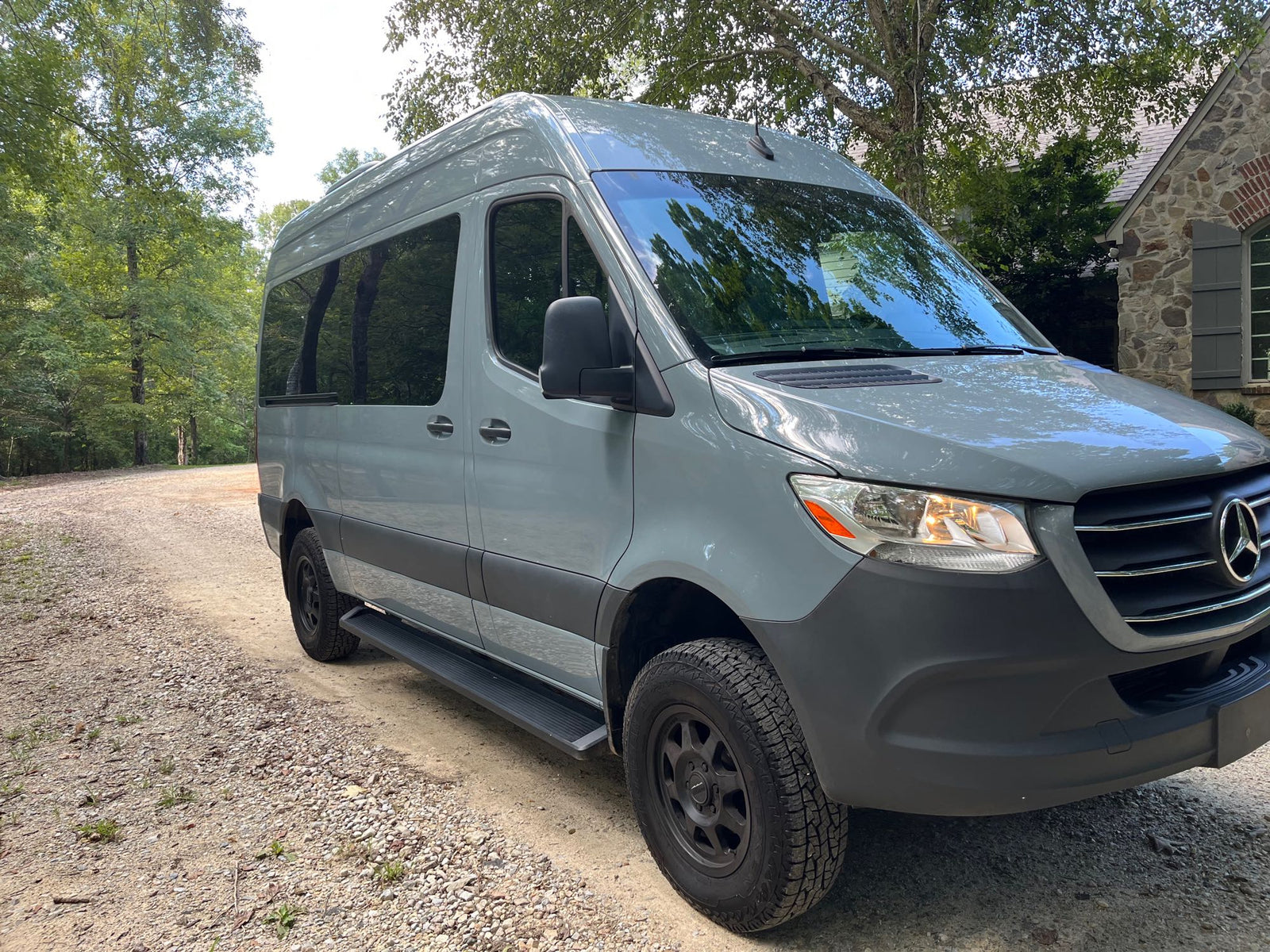 and a serene view of a forest and lake through the windows.|Spacious RV rental van interior with multiple rows of comfortable black leather seats and seatbelts for group travel.|RV rental interior: driver's view of the modern dashboard