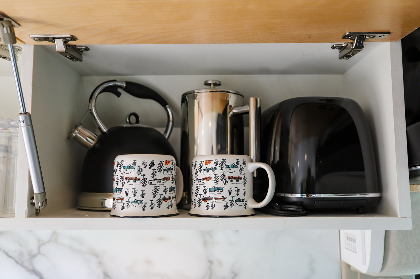 Compact RV rental kitchen cabinet. Stores kettle, French press, toaster, & mugs with RV designs. Essential amenities.