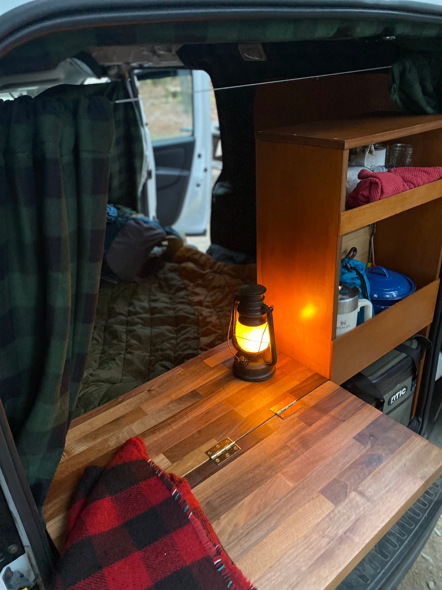 featuring camping backpacks on the driver's seat and a bed in the back.|Cozy RV rental evening: lantern glows