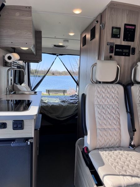 Experience serene lakeside views from this modern RV rental interior, featuring a cozy bed & kitchen. Perfect camper van.