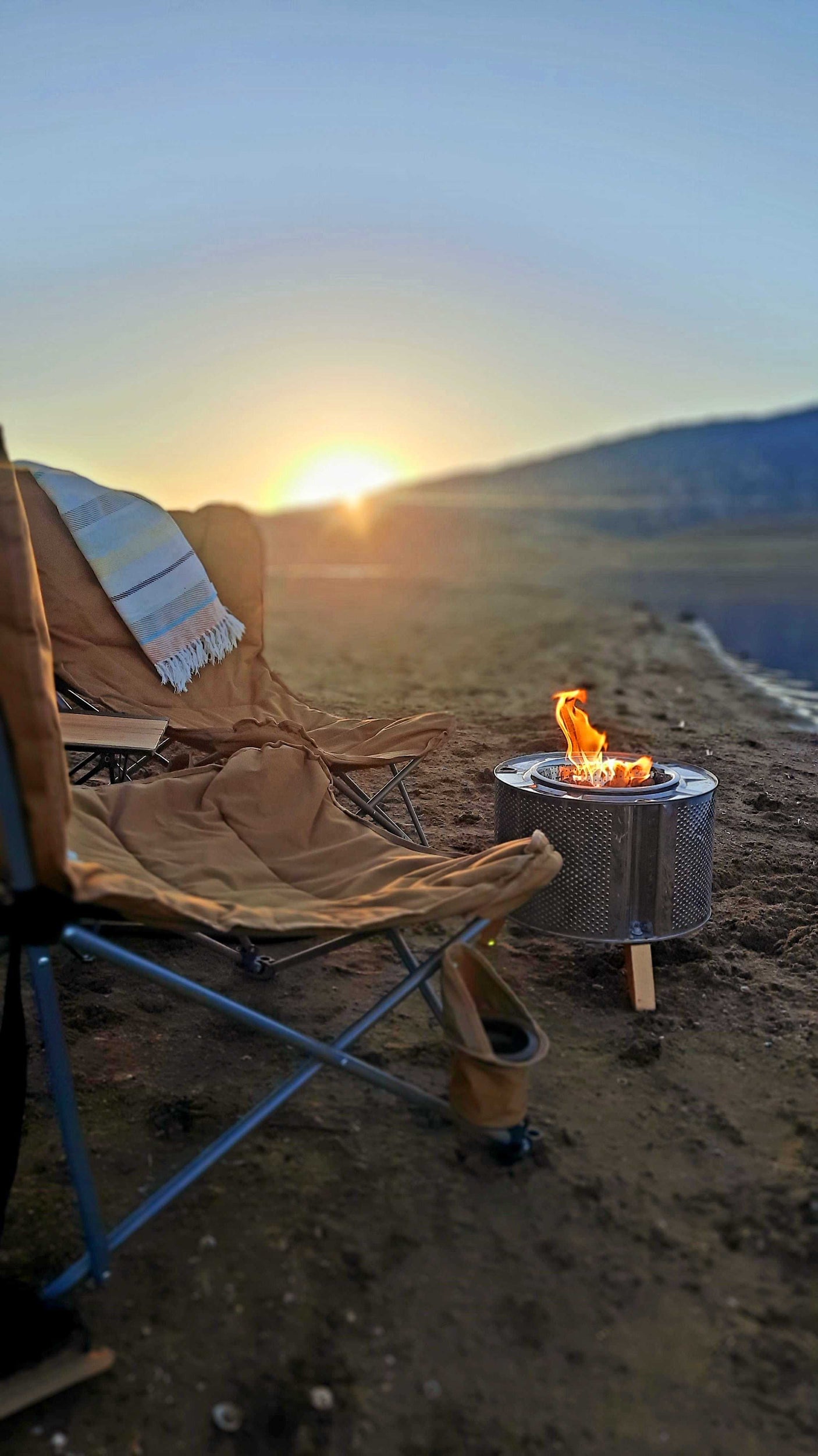 Enjoying a tranquil outdoor sunset by the lake, with comfy camping chairs and a warm fire pit. Ideal for an RV rental getaway.
