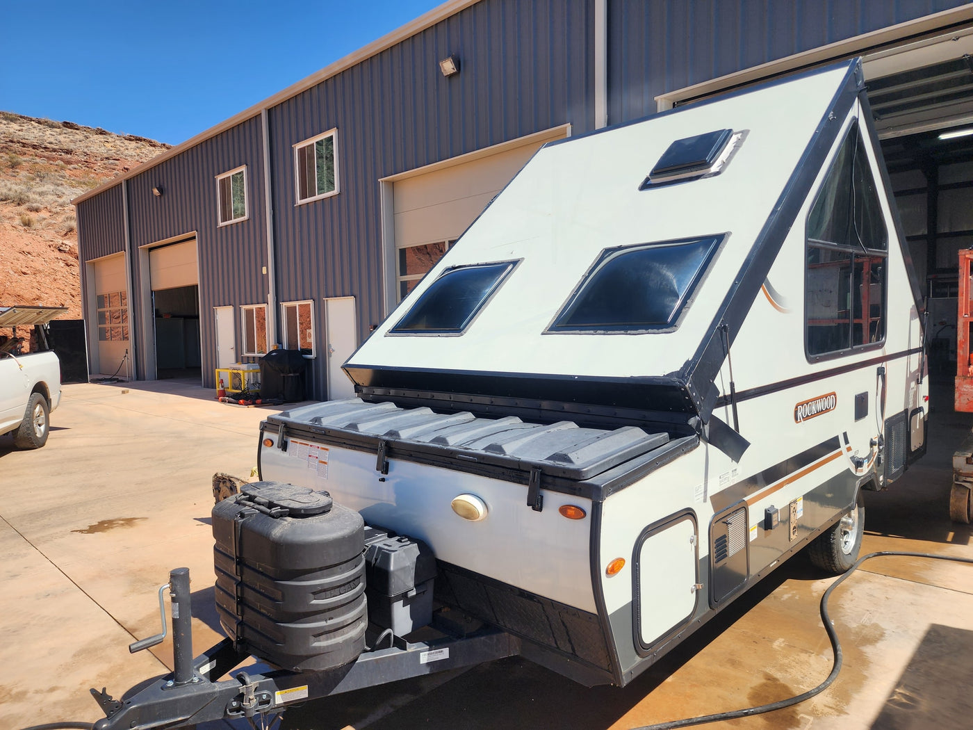 This Rockwood A-frame rv rental camper awaits adventure, parked by a shop with desert hills behind it. — photo 4