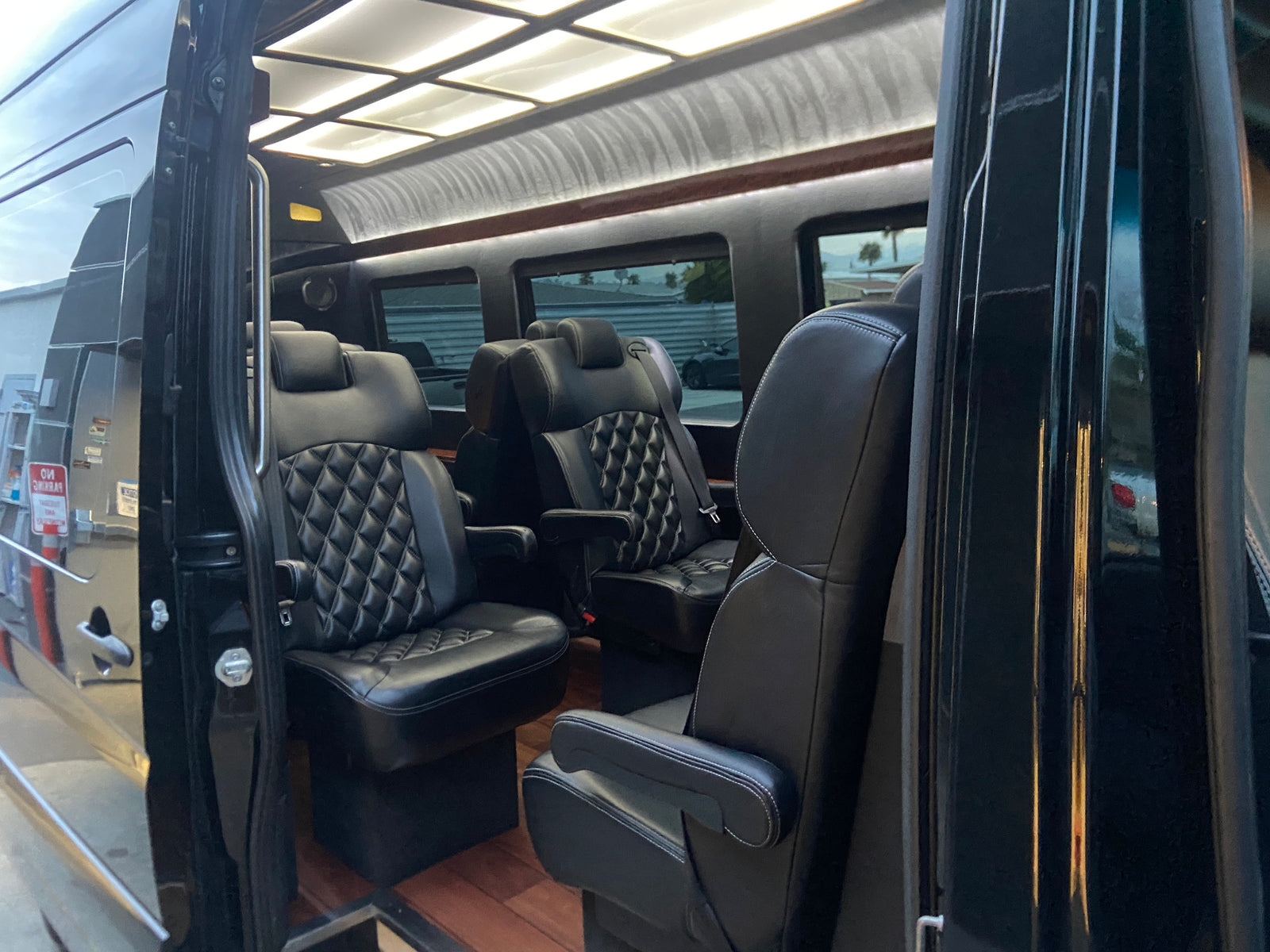 Interior of a luxury RV rental van with black quilted leather captain's chairs, wood floor, and overhead lighting.