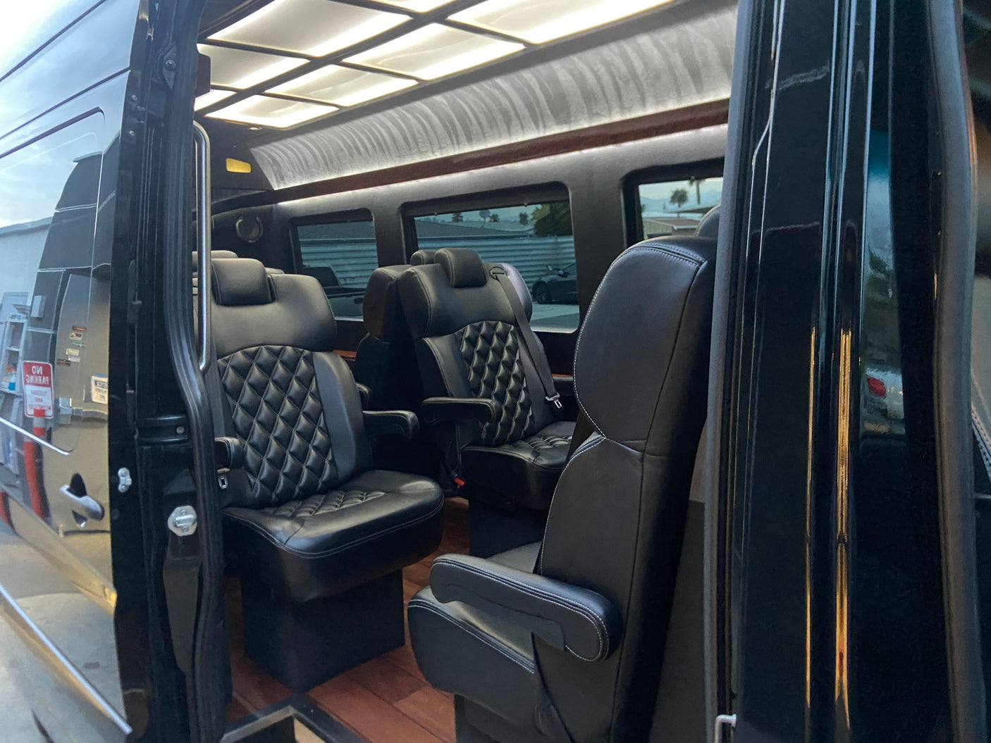 Interior of a luxury RV rental van with black quilted leather captain's chairs, wood floor, and overhead lighting.