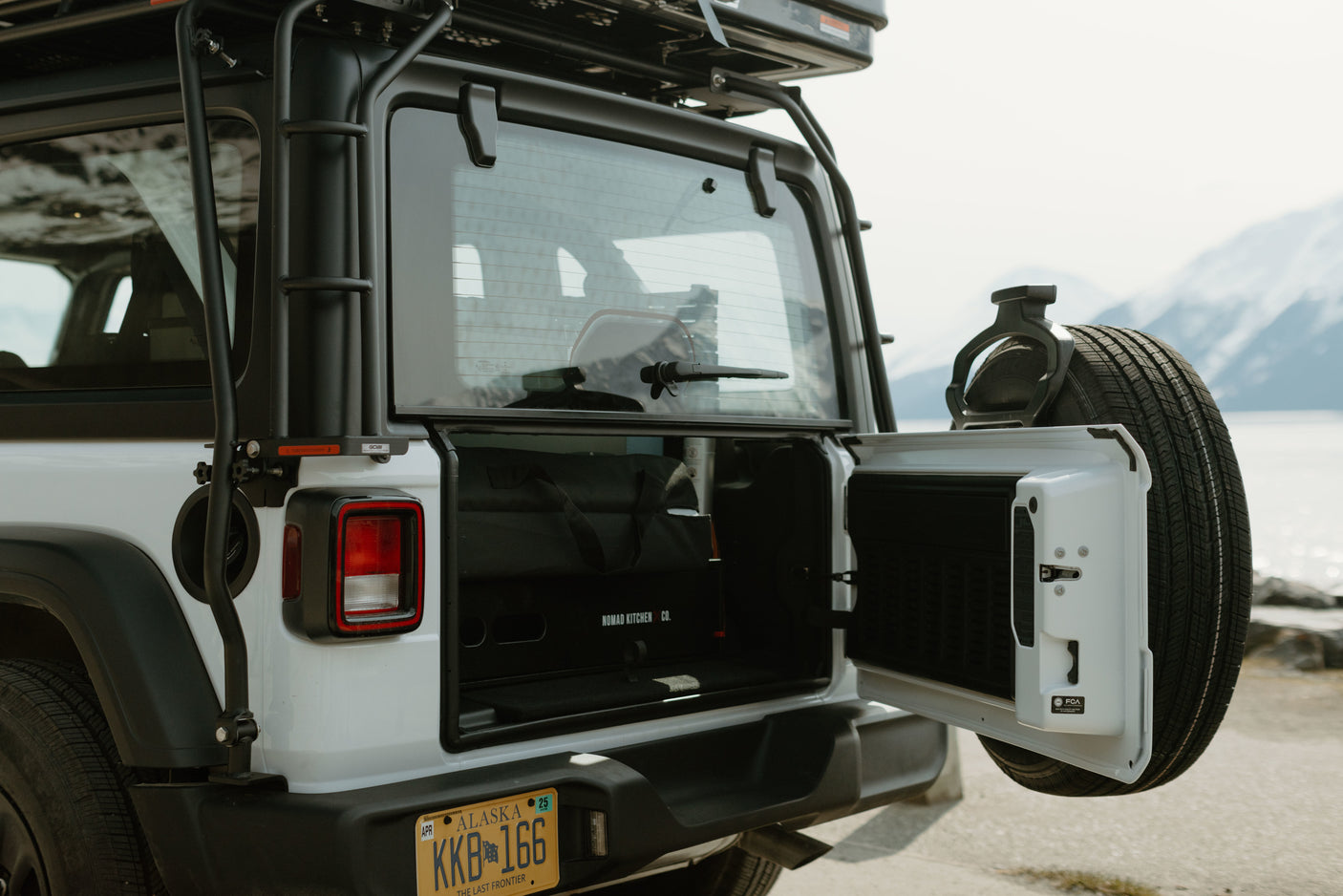 Adventure RV rental: White Jeep with open tailgate, revealing a Nomad Kitchen Co. unit. Ideal for scenic overlanding and camping.