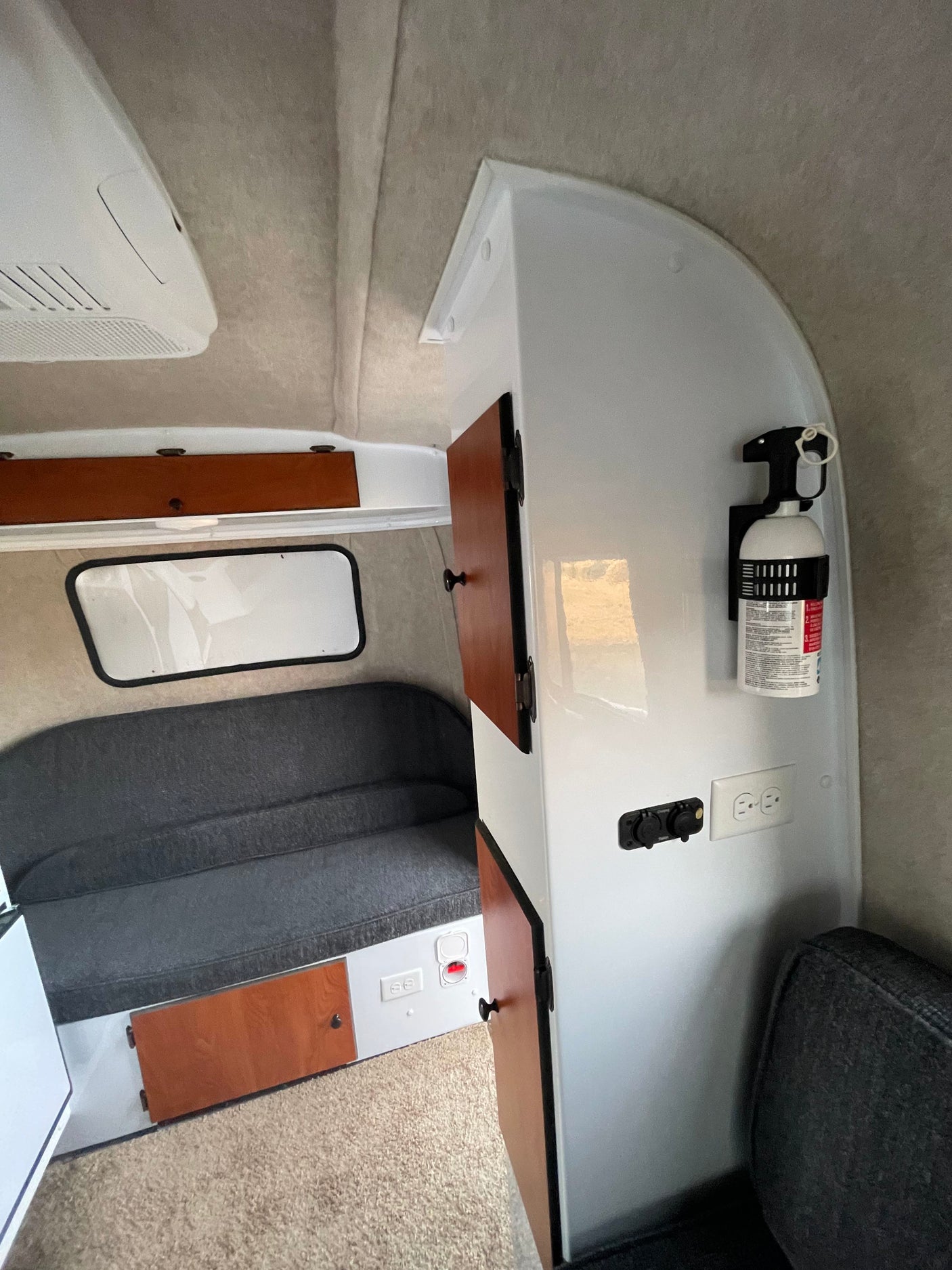 Inside a compact RV rental: bench seating, storage cabinets, AC unit, fire extinguisher, and power outlets for your journey.