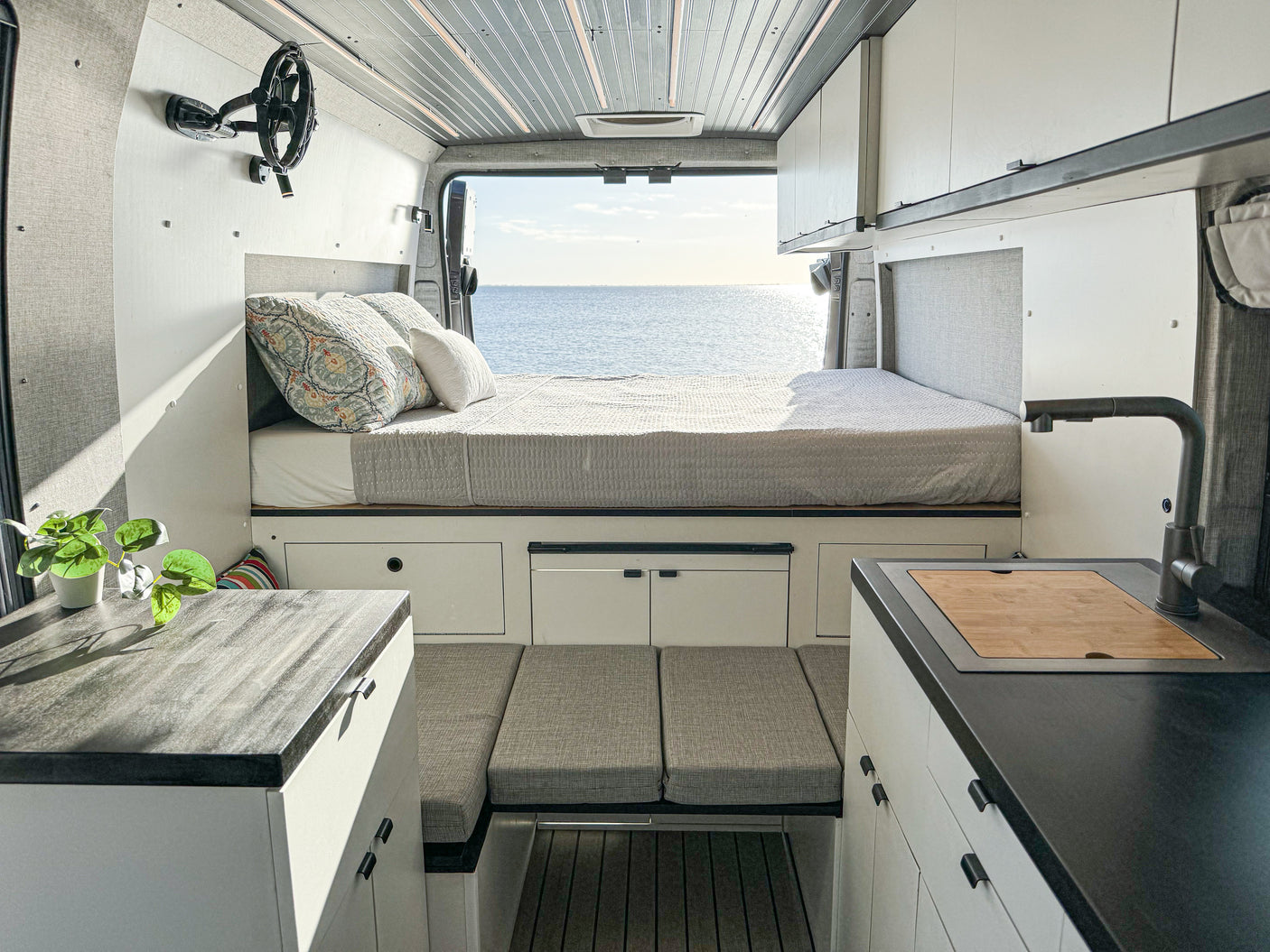 Spacious RV rental interior with a cozy bed, ocean view, modern kitchen, and comfortable living area.
