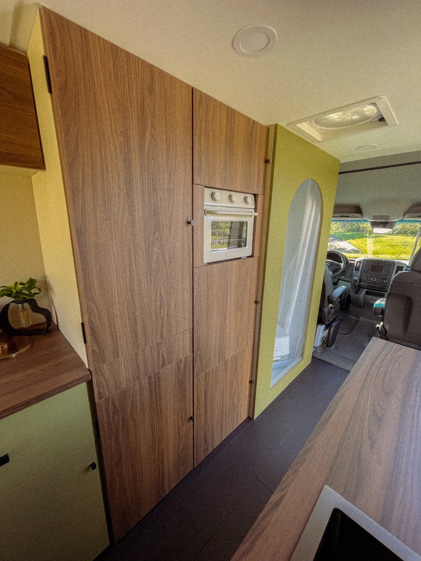 RV rental: Modern camper van interior with custom wood cabinetry, built-in oven, and a stylish green partition leading to the driver's cab. — photo 3