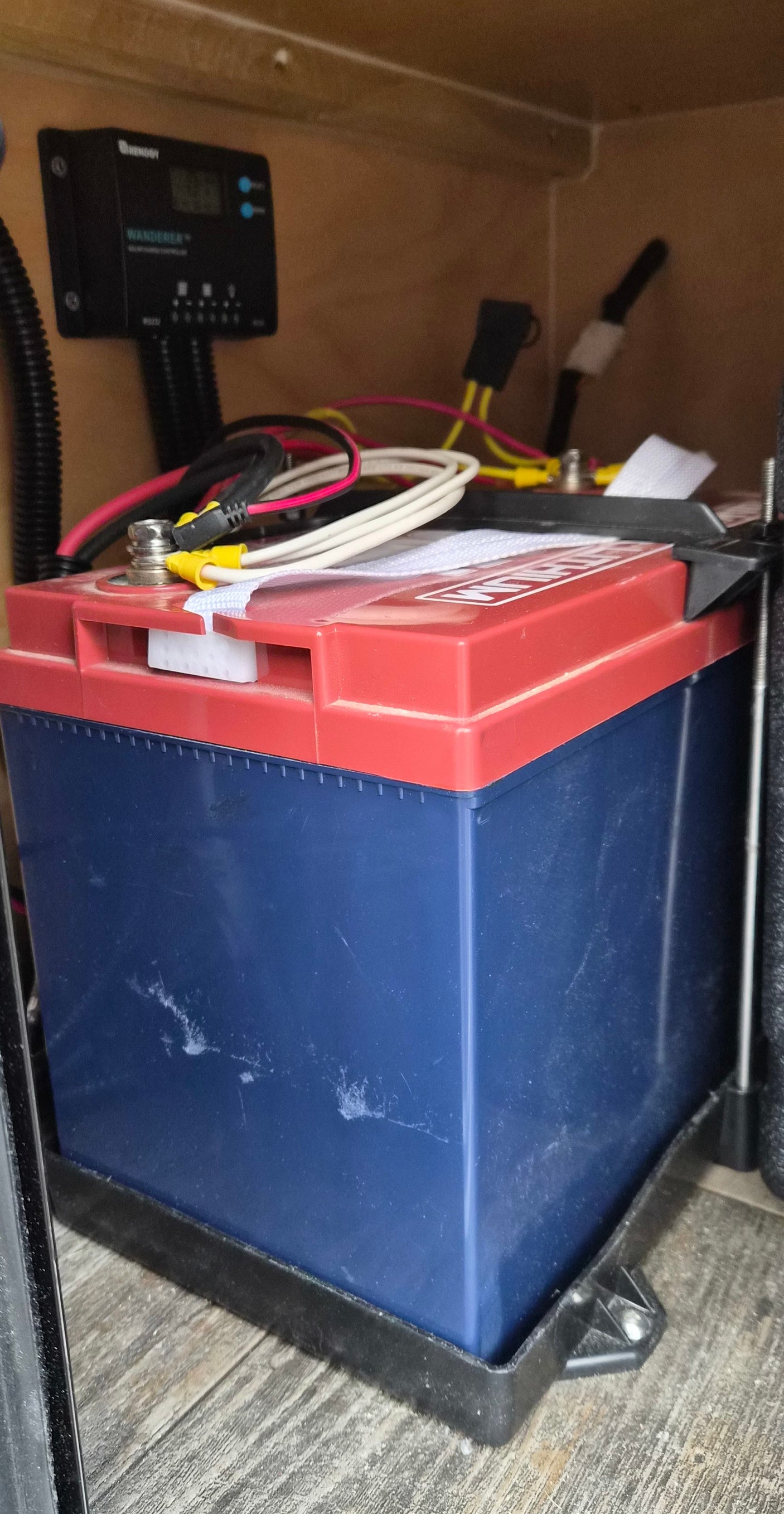 RV rental power system. Large blue & red battery with Renogy solar charge controller & wiring in a cabinet.