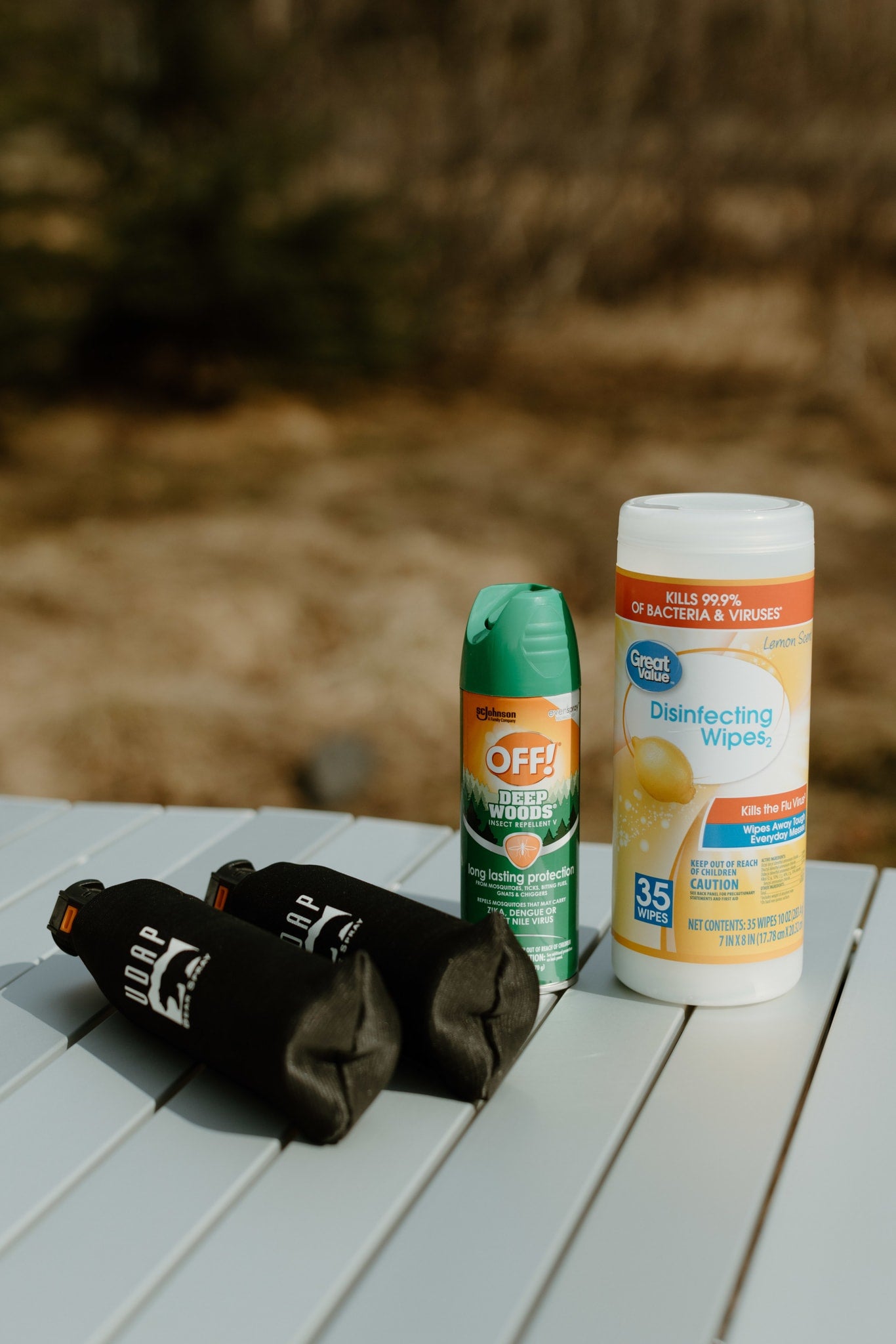 Essentials for your RV rental adventure: bear spray, bug spray, and disinfecting wipes on a camping table.