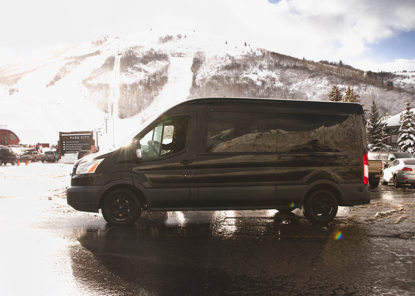 Black RV rental van at Park City ski resort. Snowy mountain slopes and ski lifts visible on a bright winter day.
