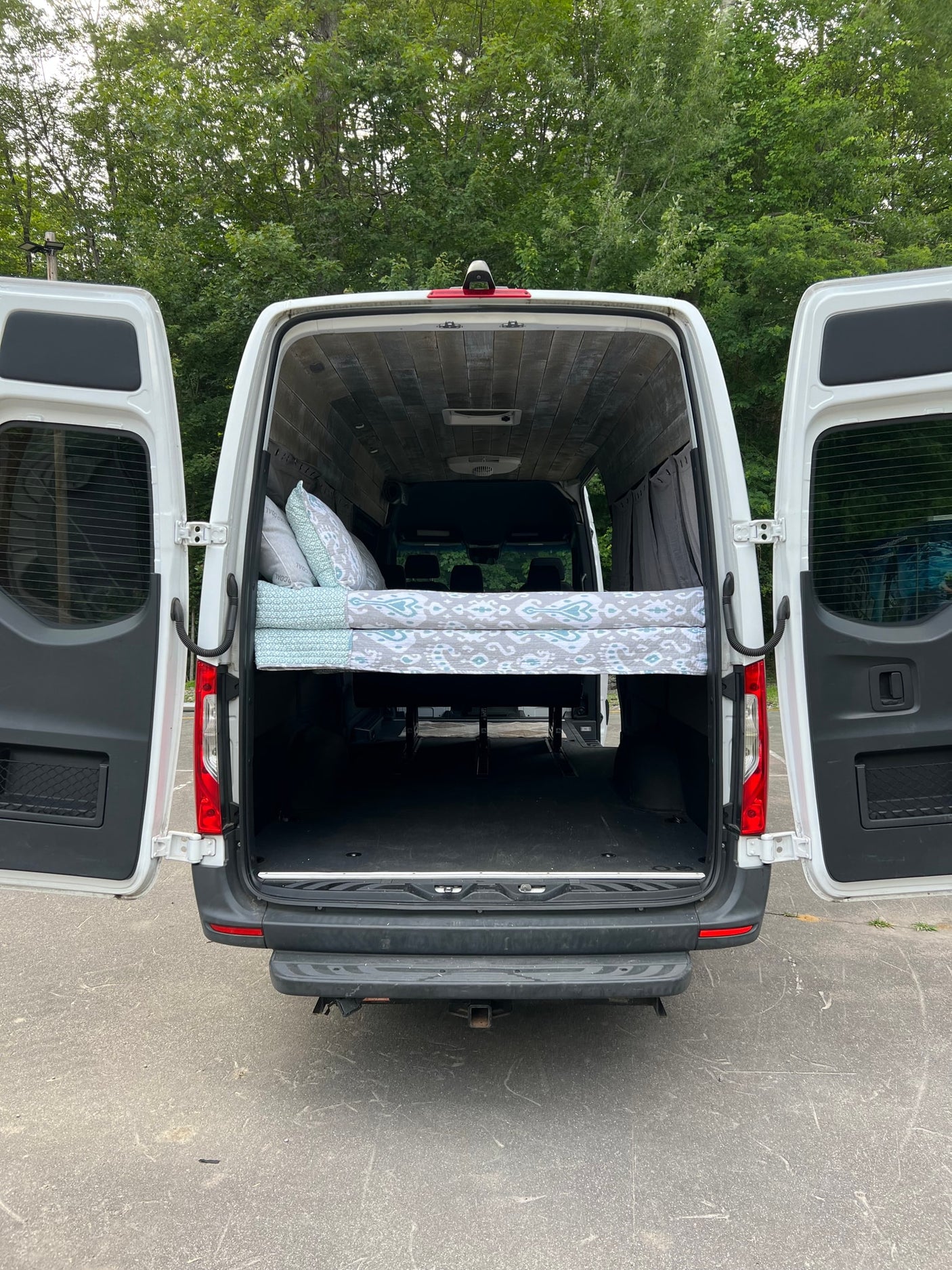 Rear view of a spacious camper van conversion. Elevated bed and ample storage visible. Ideal for rv rental.