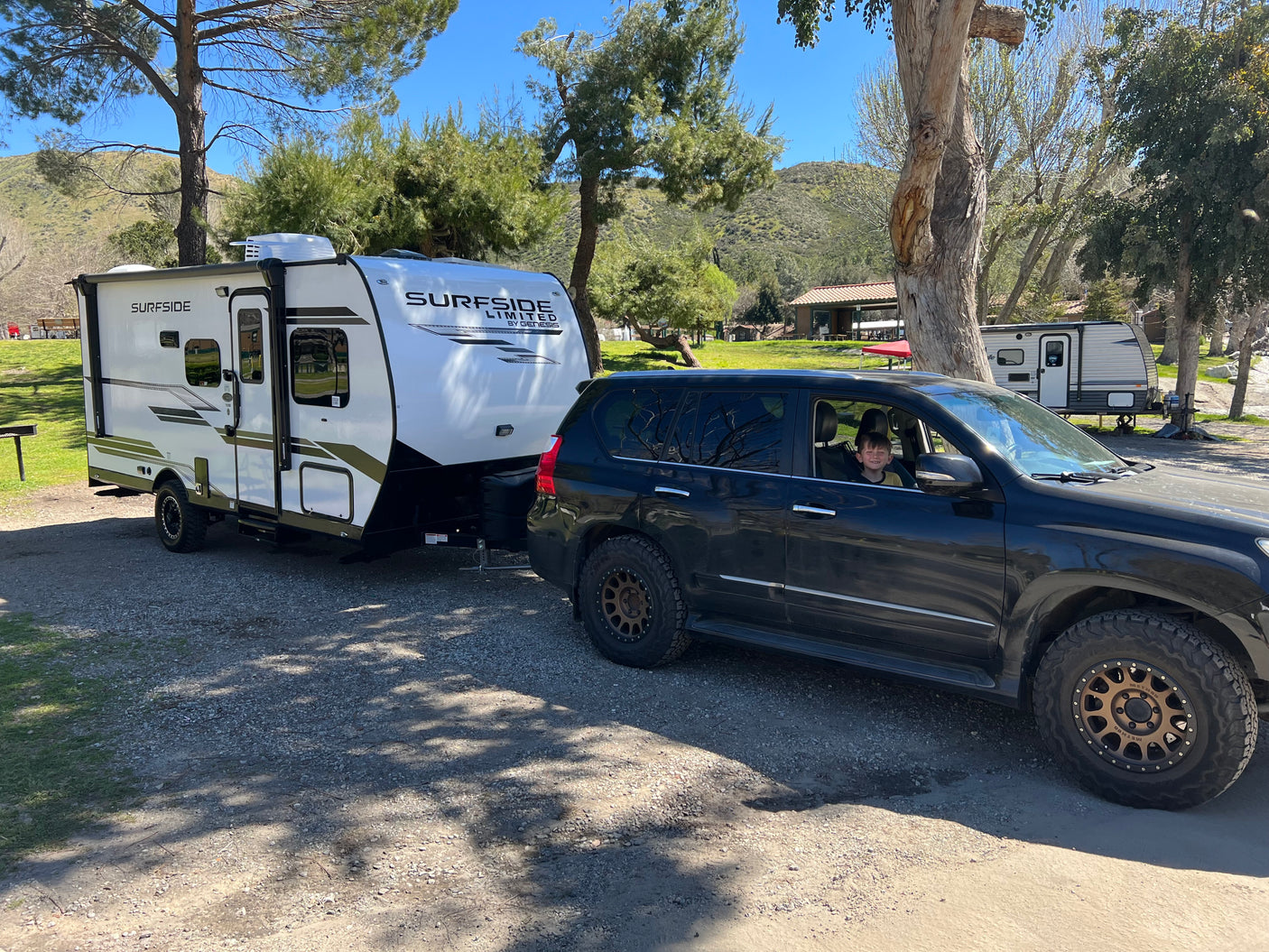 RV rental ready for a camping trip! White Surfside travel trailer hitched to a dark SUV with a child smiling from the window.